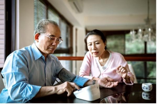 A man checking his blood pressure at home with his wife helping. 