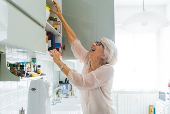 A senior women reaching into a high cabinet above her kitchen sink